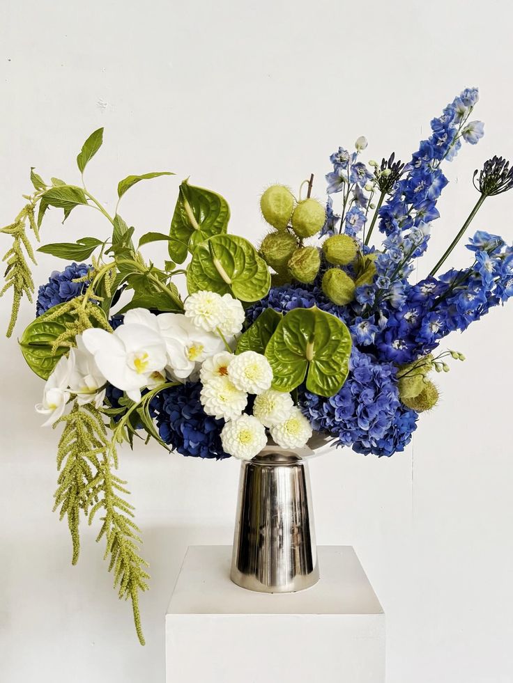 Bouquet of blue, white, and green flowers in a silver vase on a white background