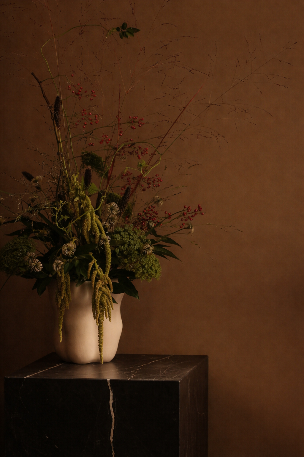 Floral arrangement in a vase on a dark surface against a brown wall