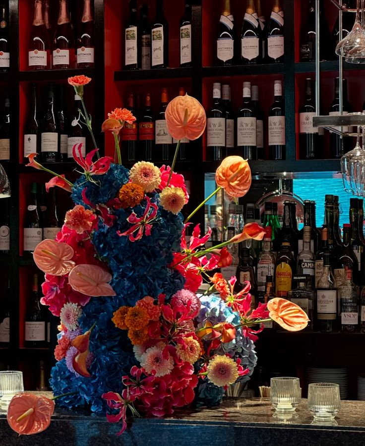 Colorful floral arrangement on a bar counter with wine bottles in the background