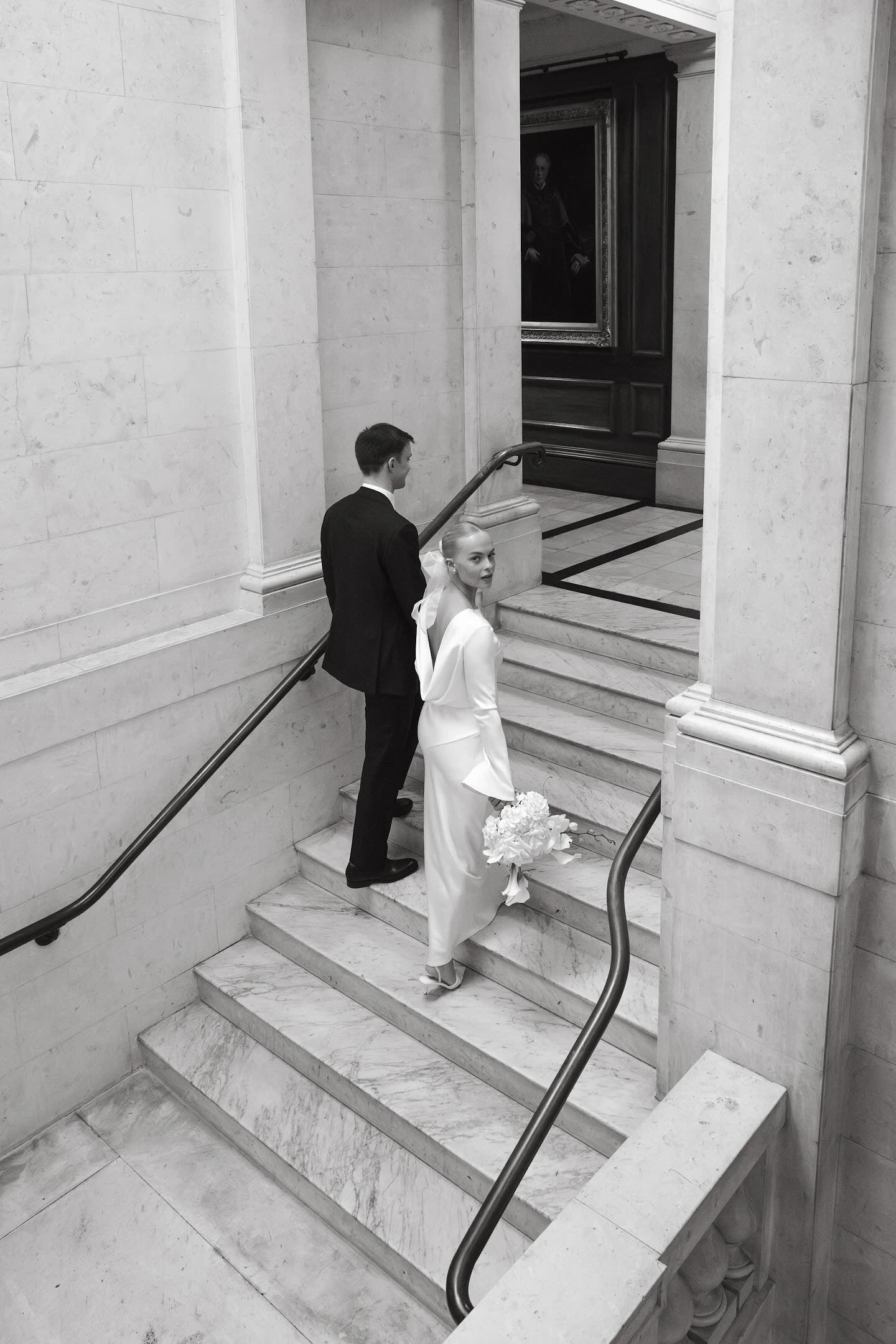 Wedded couple walking down a marble staircase in an elegant building with beautiful flower bride bouquet
