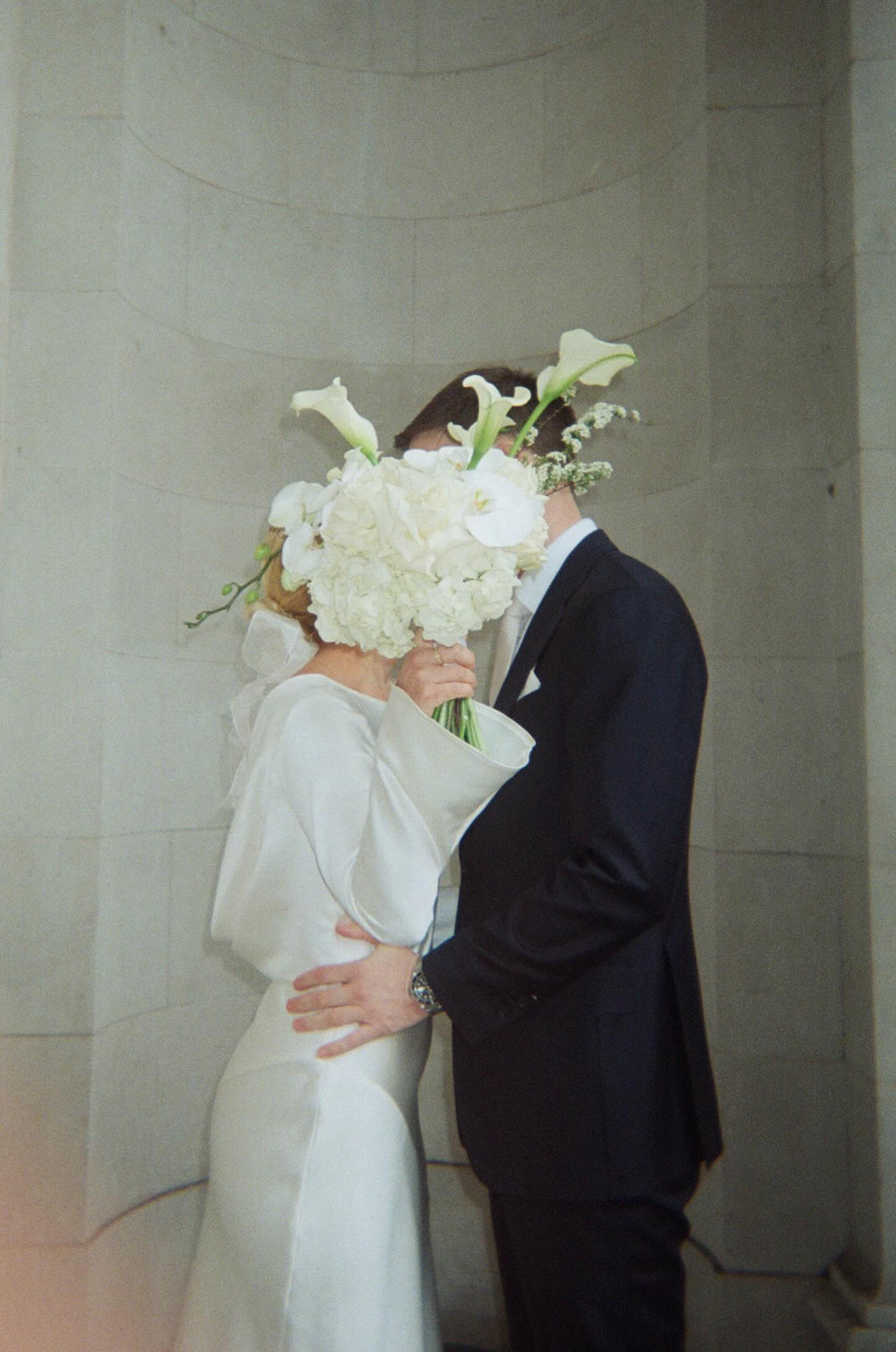 Couple embracing with a bouquet of white flowers in an indoor setting.
